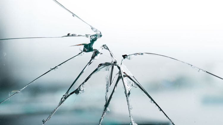 Close-up of a cracked glass surface with multiple jagged fractures radiating from a central point.